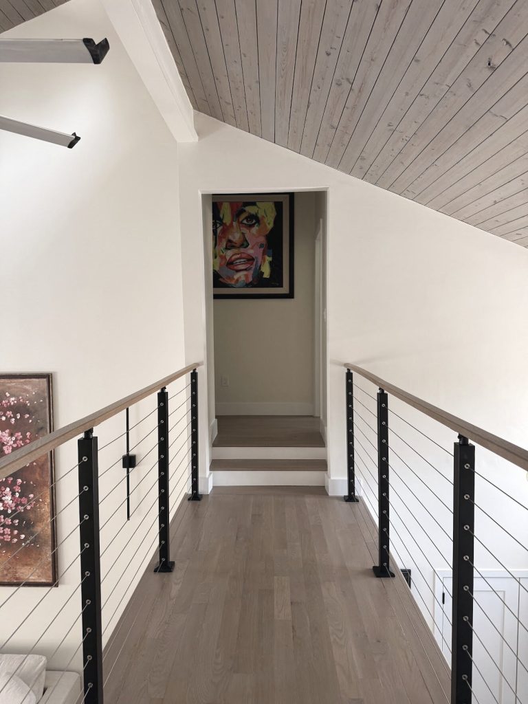 A hallway under a shiplap ceiling with a cable rail